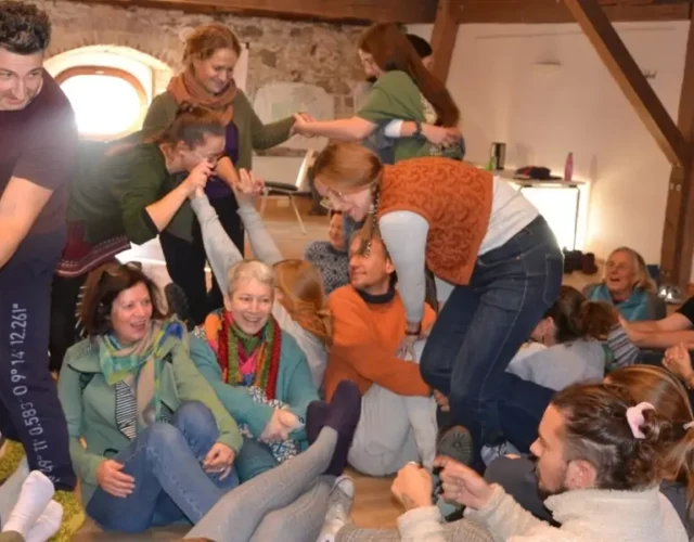 Eine größere Gruppe erwachsener Personen - zum Teil auf dem Boden sitzend oder stehend - in einem Spiel
